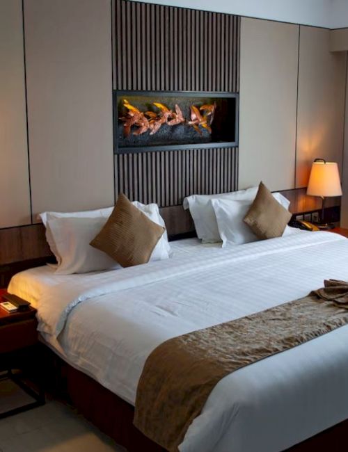 A neatly arranged hotel room with a large bed, bedside tables with lamps, a decorative wall piece, and curtains at the window, well-lit and inviting.