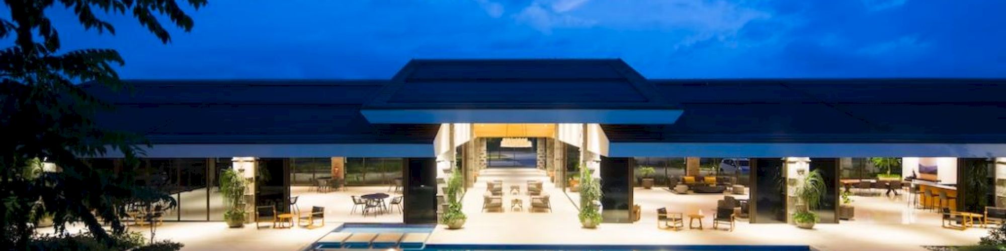 An illuminated outdoor swimming pool with a modern building in the background, set against a twilight sky, creating a serene and luxurious atmosphere.
