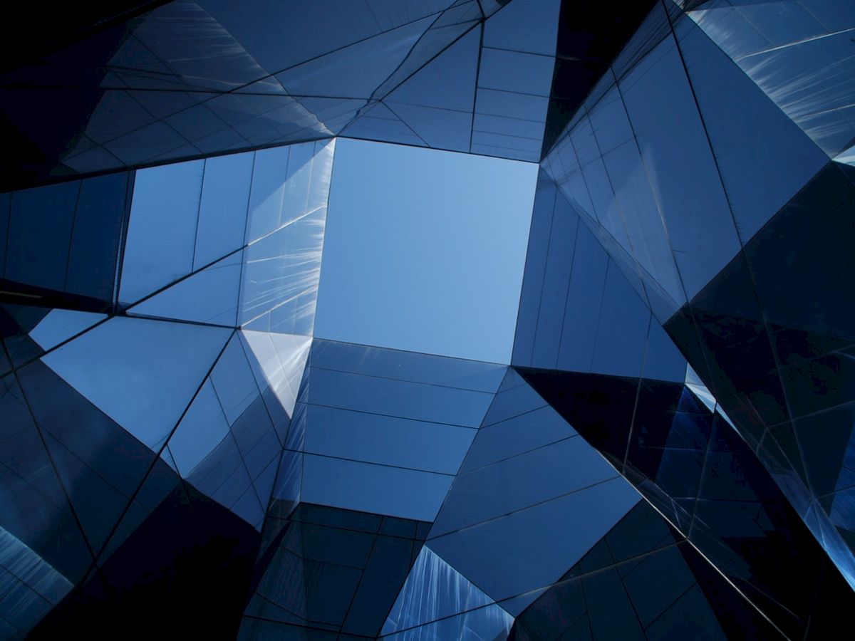 The image features an upward view of a modern, geometric building with reflective glass surfaces, creating a kaleidoscopic effect.