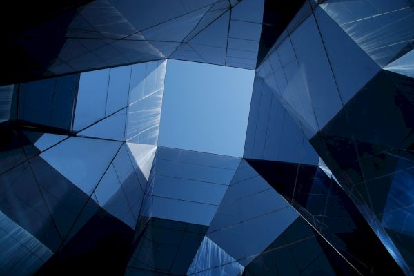The image shows a blue sky viewed through the geometric glass façade of a modern building, creating a symmetrical, abstract architectural pattern.