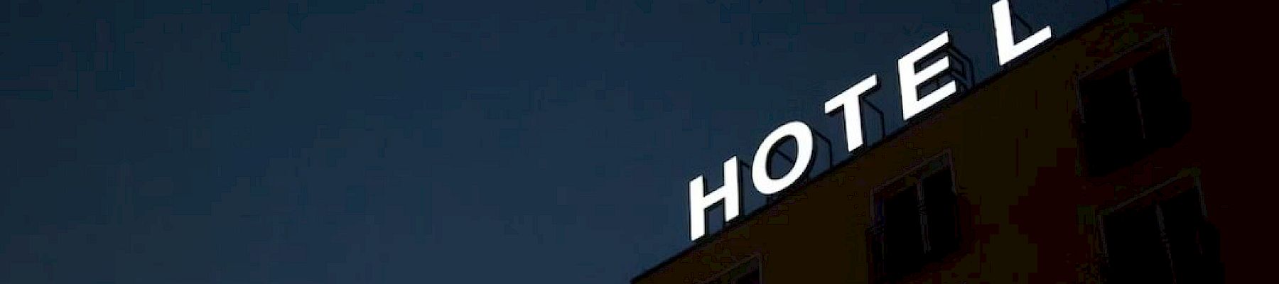 A building at night displays an illuminated "HOTEL" sign with the letter "E" not lit.