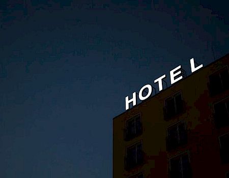 A building at night displays an illuminated "HOTEL" sign with the letter "E" not lit.
