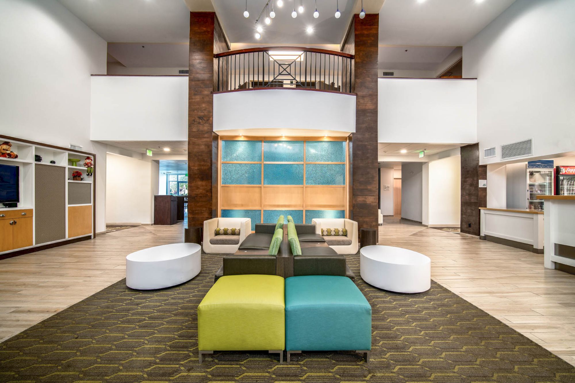 A modern lobby with colorful seating, wooden accents, and a stylish multi-panel back wall under hanging lights.