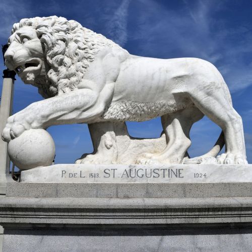 A white stone statue of a lion stands on a pedestal inscribed with 