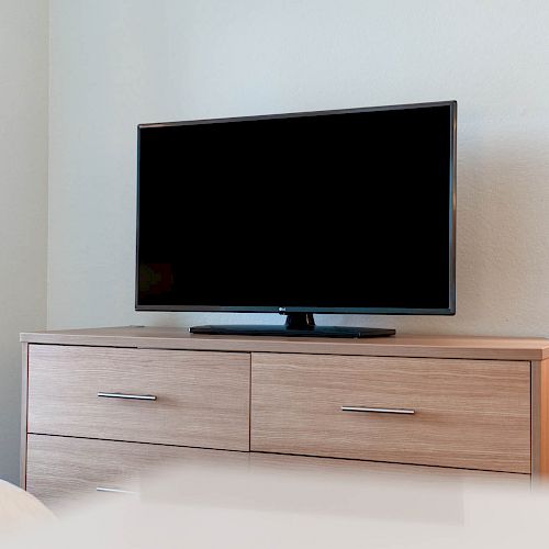 The image shows a flat-screen TV placed on a wooden dresser with drawers against a light-colored wall.