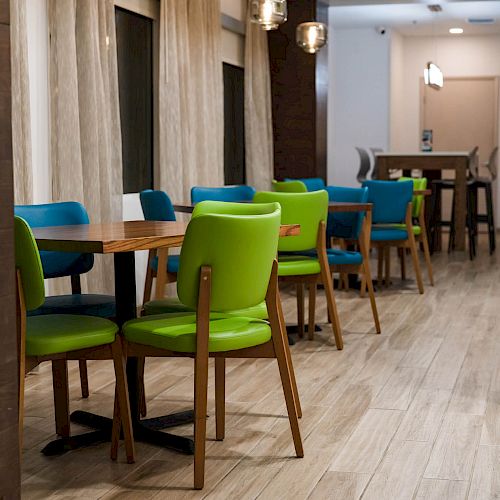 This image shows a modern dining area with wooden tables, green and blue chairs, and a tiled wall. It appears to be well-lit and inviting.