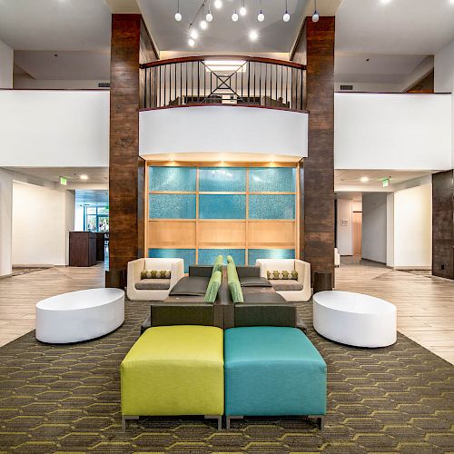 This image features a modern lobby with colorful seating, a carpeted area, a central decorative wall, and contemporary light fixtures.