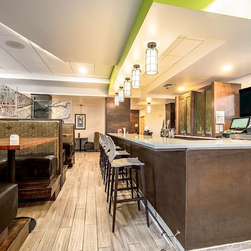 The image shows a modern restaurant interior featuring a bar counter with stools and booth seating along the side.