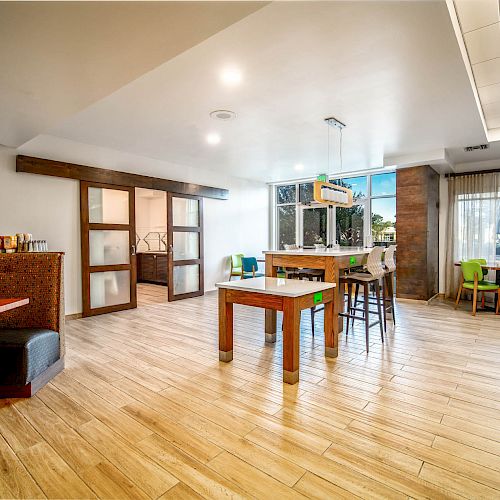 This image shows a modern, spacious dining area with wooden floors, various seating options, and large windows letting in natural light.