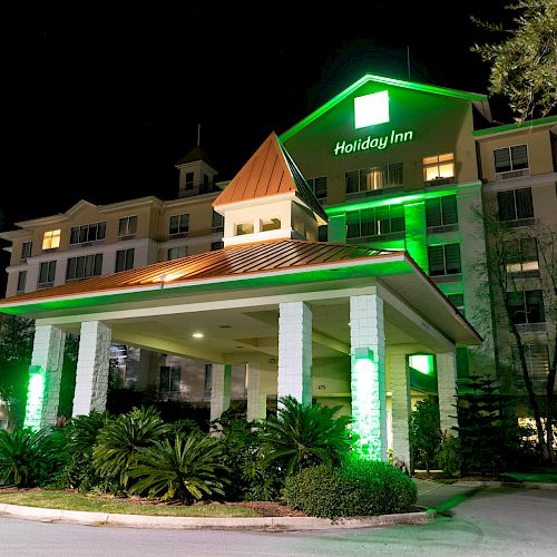 A Holiday Inn hotel is shown at night, illuminated with green lighting around the entrance and landscaping.