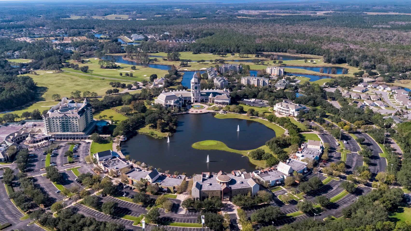 The image shows an aerial view of a community with a circular layout around a central lake, surrounded by buildings, roads, and greenery.