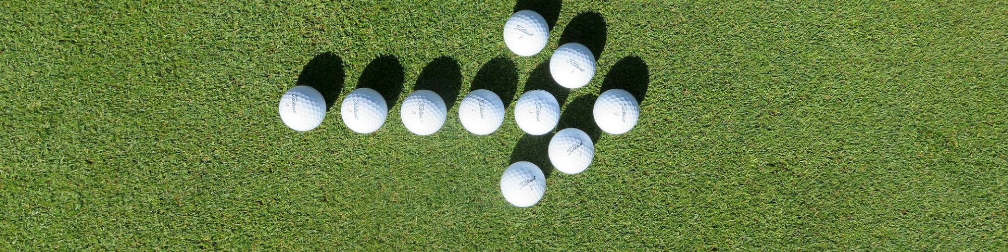 The image shows a group of golf balls arranged on a green grassy surface to form an arrow pointing to the right.