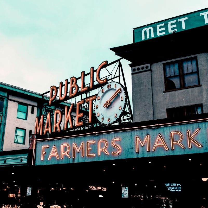The image shows a famous Public Market and Farmers Market sign with a clock in a vibrant urban area, with surrounding buildings and signage.