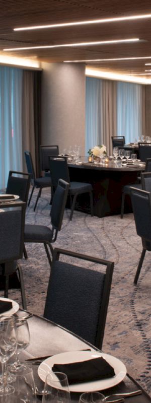 A banquet hall with round tables set for a formal event; tables are adorned with glassware, cutlery, napkins, and floral centerpieces.