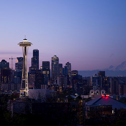 The image shows the Seattle skyline at dusk, with the Space Needle prominently featured and Mount Rainier visible in the background.