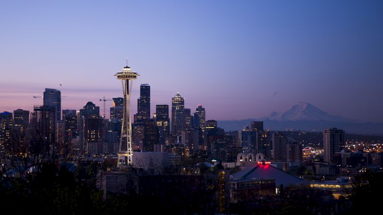 A twilight view of Seattle's skyline featuring the Space Needle with Mount Rainier visible in the background, and city lights beginning to shine.